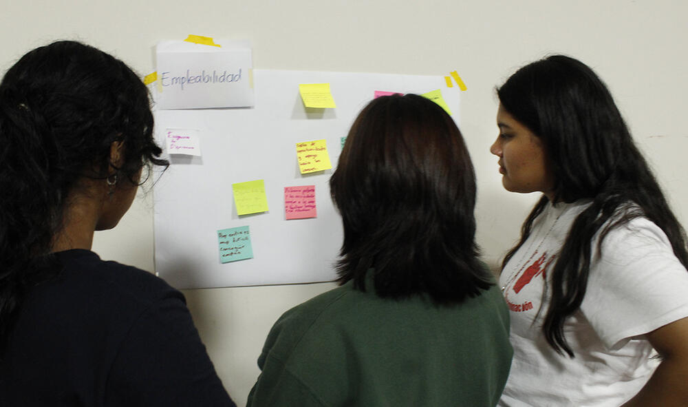 Jóvenes conversan frente a un papelógrafo diversas acciones que pueden implementar en su comunidad.