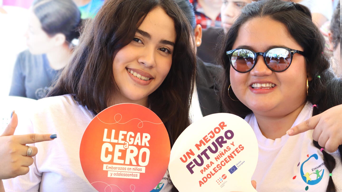 Dos jóvenes sonriendo señalan abanicos con la leyenda: "Llegar a Cero embarazos en niñas y adolescentes".